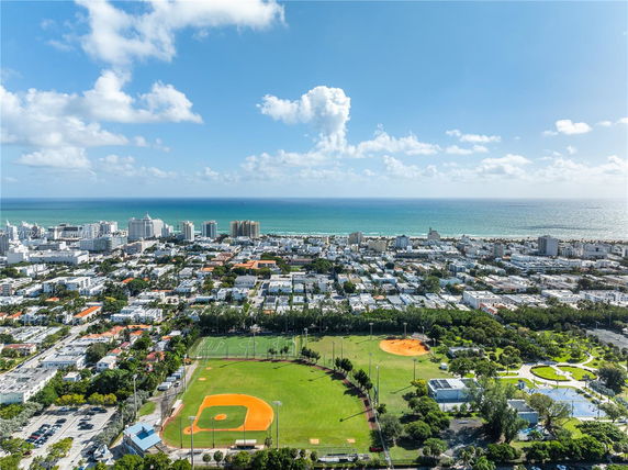 Panoramic view of a cityscape with sports fields in the foreground and ocean in the distance.