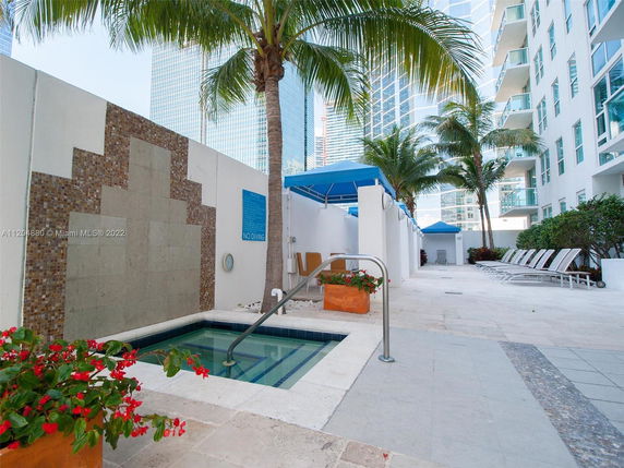 Outdoor swimming pool area with lounge chairs and palm trees next to a building.