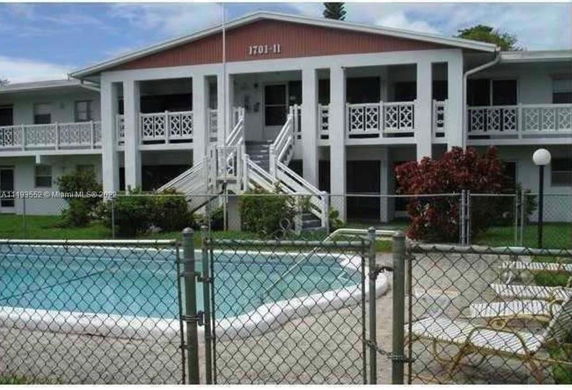 Front view of a two-story building with a swimming pool enclosed by a fence.