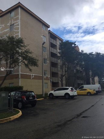 Front view of a multi-story apartment building with vehicles parked in front.