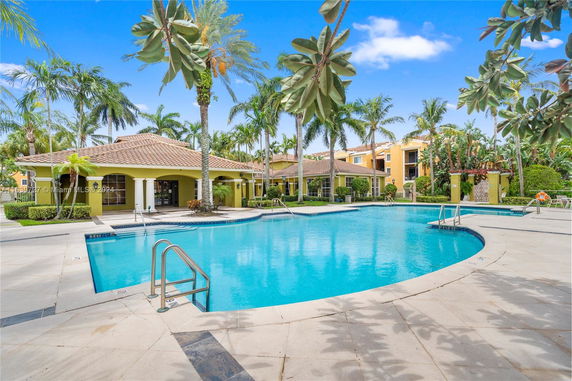 Outdoor swimming pool area with surrounding palm trees and a building with a tiled roof.
