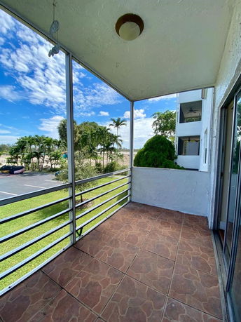 Balcony view overlooking a parking area with a grassy lawn and trees.