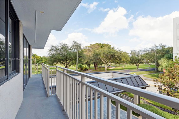 Balcony view overlooking a landscaped area with trees and a road.