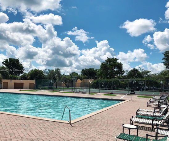 Outdoor swimming pool area with lounge chairs and nearby tennis courts.
