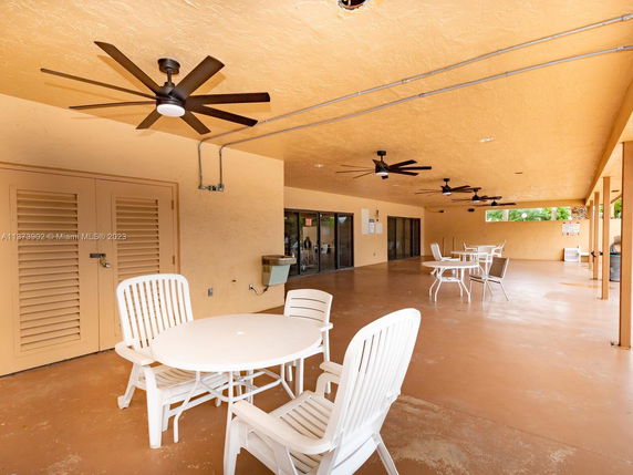 Indoor recreational area with tables and chairs, featuring ceiling fans.