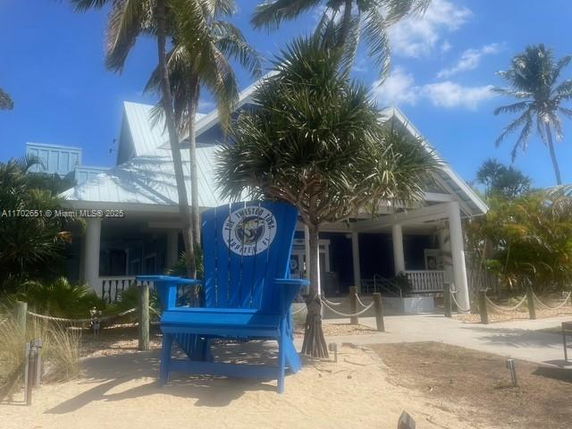 Front view of a house with a large blue chair in the foreground and palm trees surrounding it.