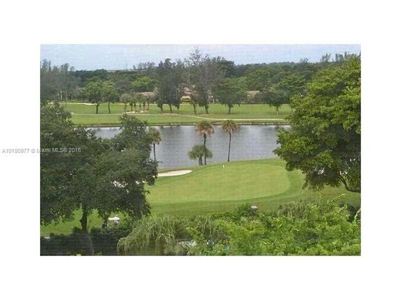 View of a lake and a golf course with trees and greenery in the background.