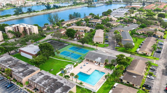 Aerial view of a residential area with tennis courts and a swimming pool, adjacent to a body of water.