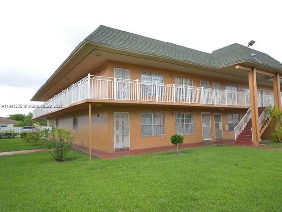 Front view of a two-story building with a wraparound balcony and a green lawn.