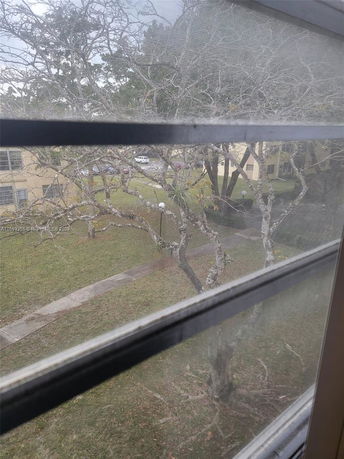 View through a window showing trees and a nearby building structure with a parking area.