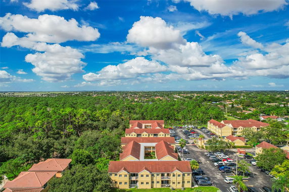 Aerial view of residential buildings with red roofs surrounded by dense greenery and a parking area.