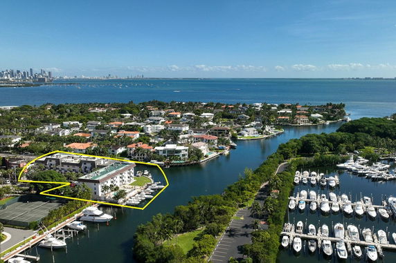 Aerial view of a coastal residential area with a marina, showing various houses, buildings, and yachts along waterways.