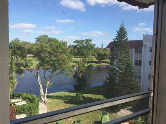 View of a lush landscape with a pond, trees, and a multi-story building.