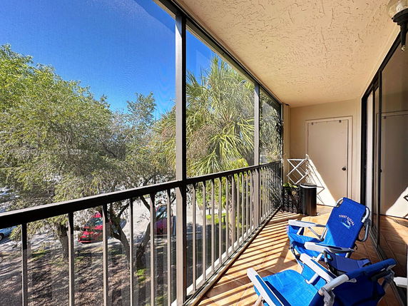 View from a balcony with trees and a parking area visible through a screened enclosure.