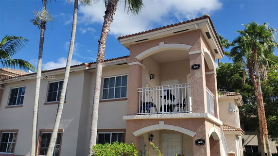 Front view of a two-story building with balconies and palm trees nearby.