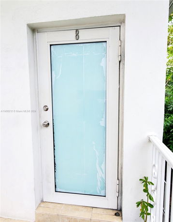 Exterior view of a door with frosted glass panel set in a white wall.