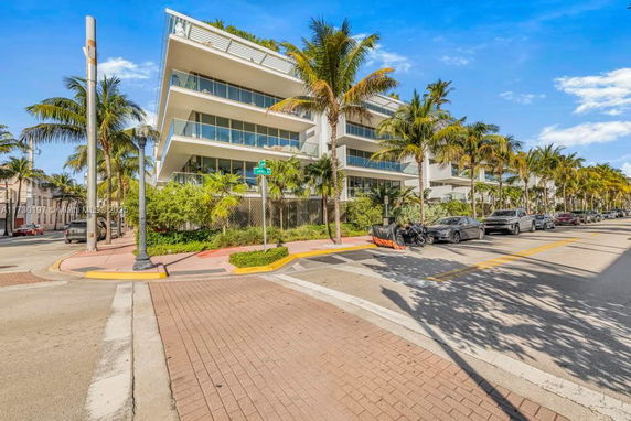 Front view of a modern multi-story building with palm trees along the sidewalk.