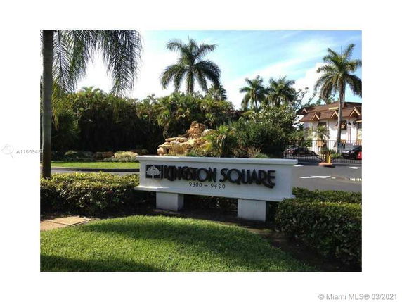 Sign for Kingston Square with palm trees and a landscaped area in the background.
