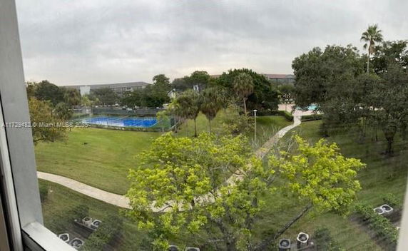 View of a grassy outdoor area with a tennis court and surrounding trees.