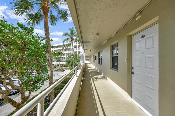 Exterior walkway of a residential building with doors and windows, overlooking a parking area and surrounding greenery.