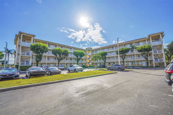 Front view of a multi-story residential building with balconies and parking area at the foreground.