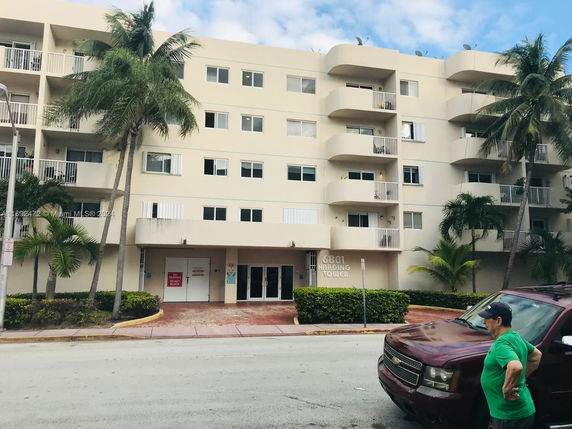 Front view of a multi-story building with balconies and palm trees.