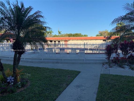 View of a swimming pool surrounded by a white fence with seating areas visible inside.