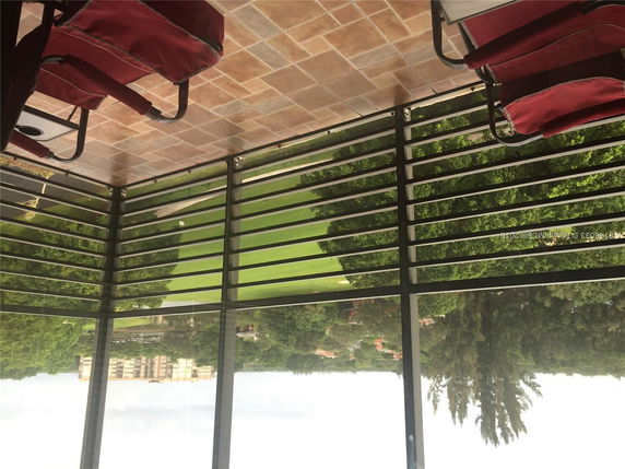 Panoramic view from a building's balcony with tiled floors and outdoor seating, overlooking green fields and distant buildings.