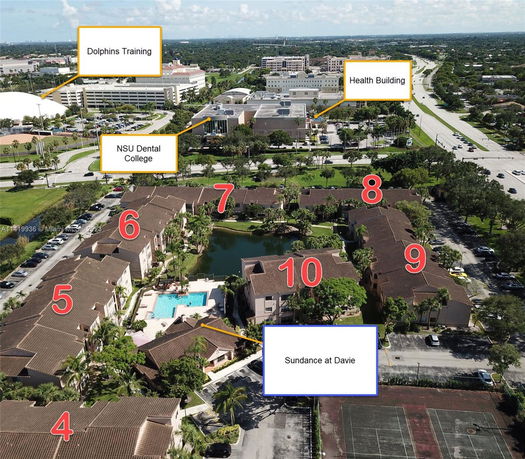 Aerial view of a residential complex with multiple buildings, a central swimming pool, and nearby educational and health facilities.