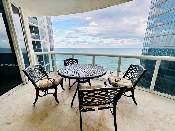 Balcony with metal furniture overlooking the ocean and nearby buildings.