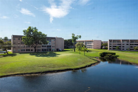 View of multiple apartment buildings with surrounding greenery and a pond.