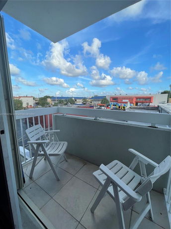 View from a balcony with two chairs overlooking buildings and a blue sky.