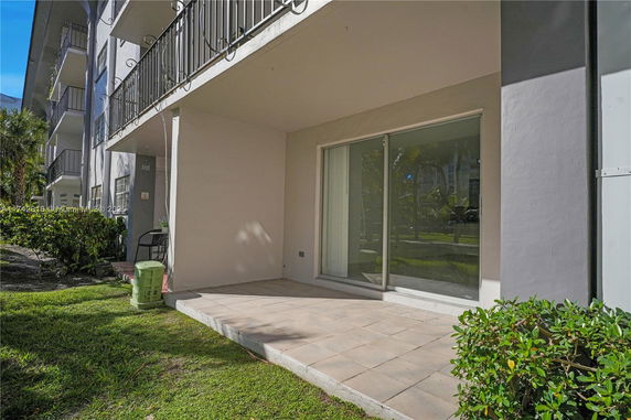 View of a building with multiple balconies and a ground-level patio with sliding glass doors.