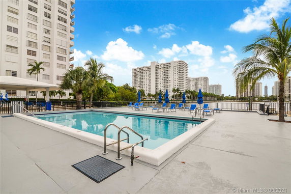 Outdoor swimming pool area with nearby high-rise buildings and palm trees.