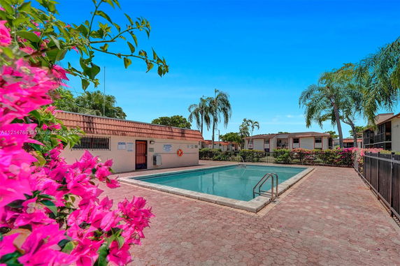 Outdoor swimming pool with surrounding buildings and tropical plants.