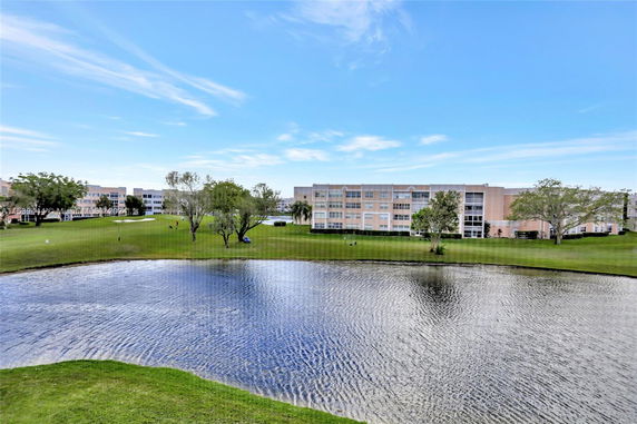 View of apartment buildings across a pond with green lawn areas.