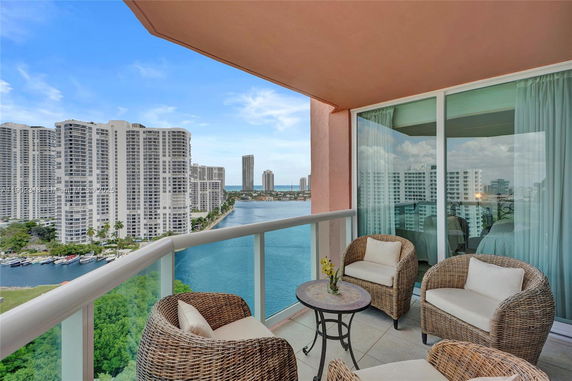 Balcony with wicker chairs and a table overlooking high-rise buildings and waterway.