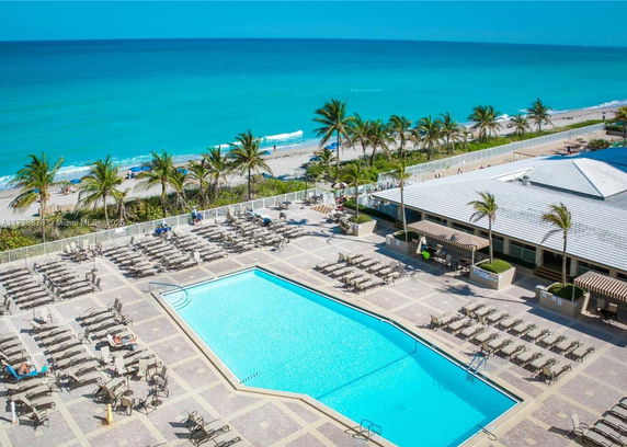 Outdoor swimming pool area with lounge chairs and beachfront view.