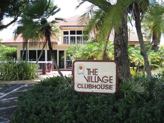 Front view of a building labeled as The Village Clubhouse with large windows and a red-tiled roof.