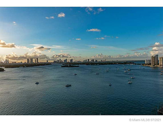 Panoramic view of a waterfront with numerous boats and a city skyline in the background during sunset.
