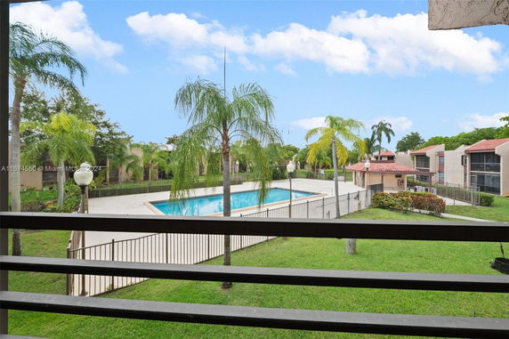 View of an outdoor swimming pool surrounded by palm trees and residential buildings.