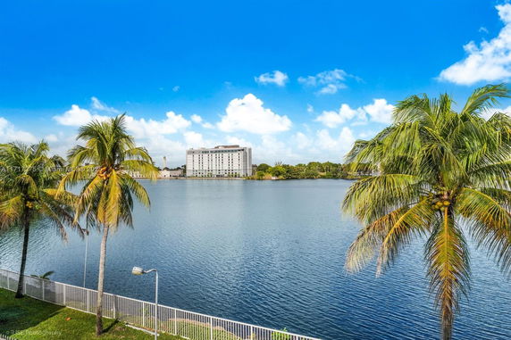 View of a large water body with a building in the distance and palm trees along the shoreline.