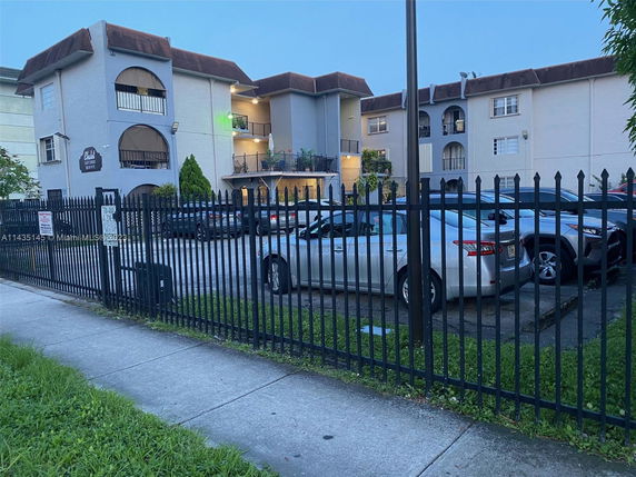 Front view of a multi-story residential building with several balconies and a parking area in front.