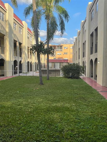 View between two rows of multi-story buildings with grass and palm trees in the center.