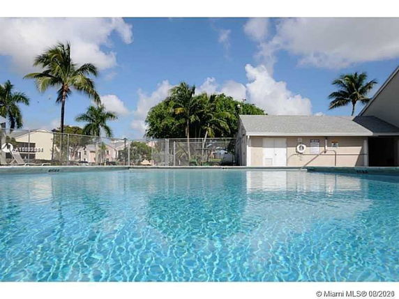 Outdoor swimming pool area with adjacent building and palm trees.