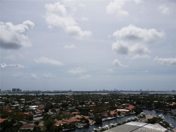 Panoramic view of a residential area with houses, trees, and a waterway, looking towards the distant city skyline.