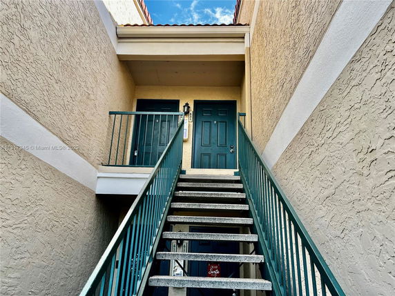 Front view of a building entrance with stairs leading to a doorway on an upper level.