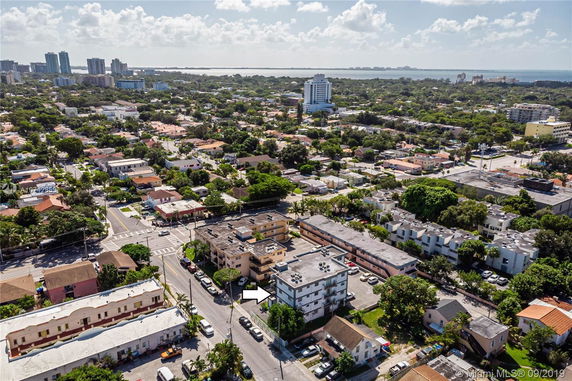 Aerial view of a residential area with various buildings and greenery, and a distant view of the sea.