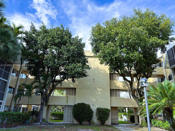 Front view of a multi-story beige building with trees in front.