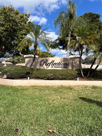 Front view of an entrance sign for Reflections at Pembroke Pines with palm trees in the background.